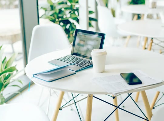 a desk with a laptop, notebook, coffee and smartphone